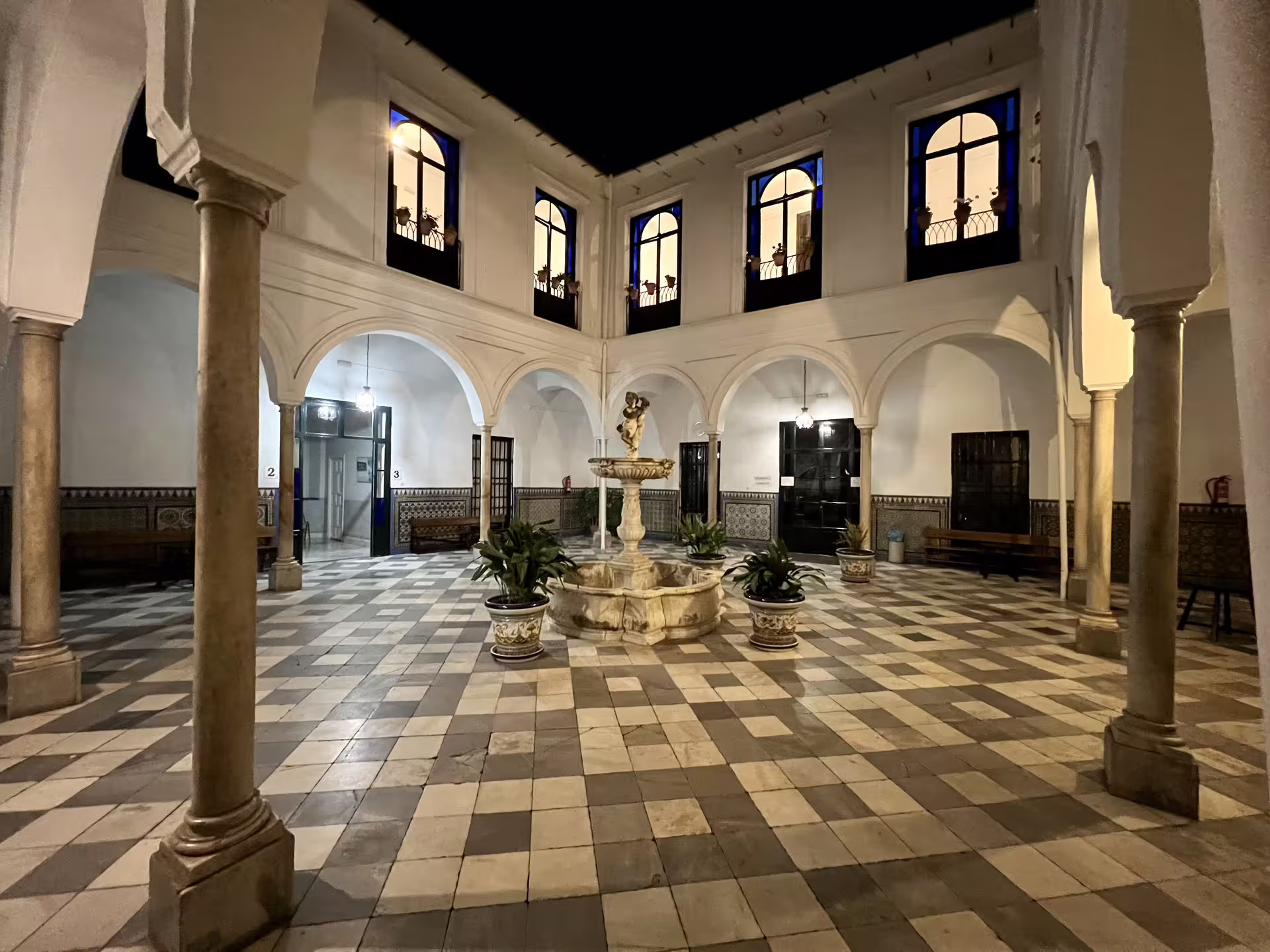 Elegant courtyard with arches and fountain illuminated at night, part of Seville's Mysterious and Paranormal Tour experience.