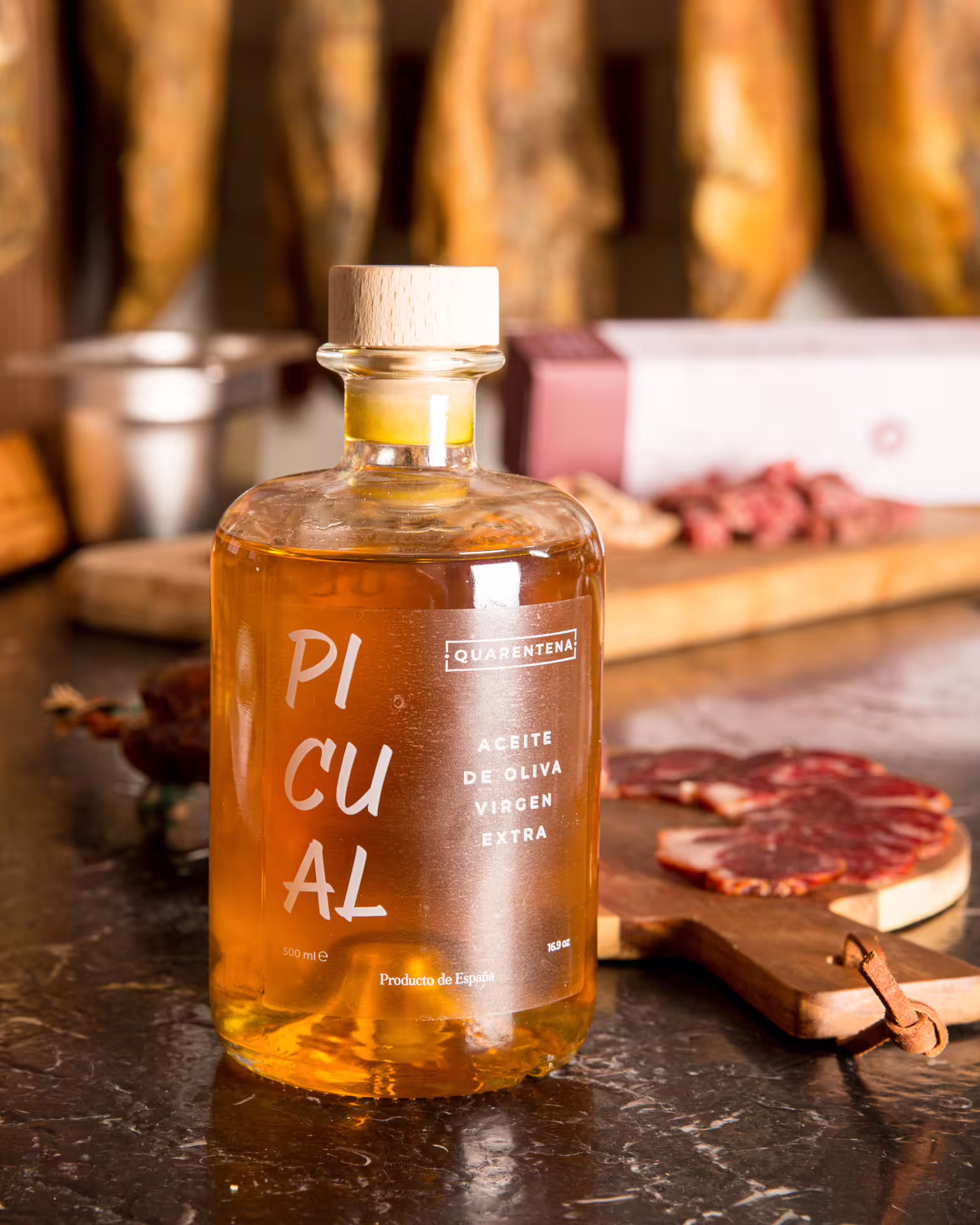Close-up of premium Picual extra virgin olive oil bottle with cured meats in rustic Seville kitchen setting during food tour.