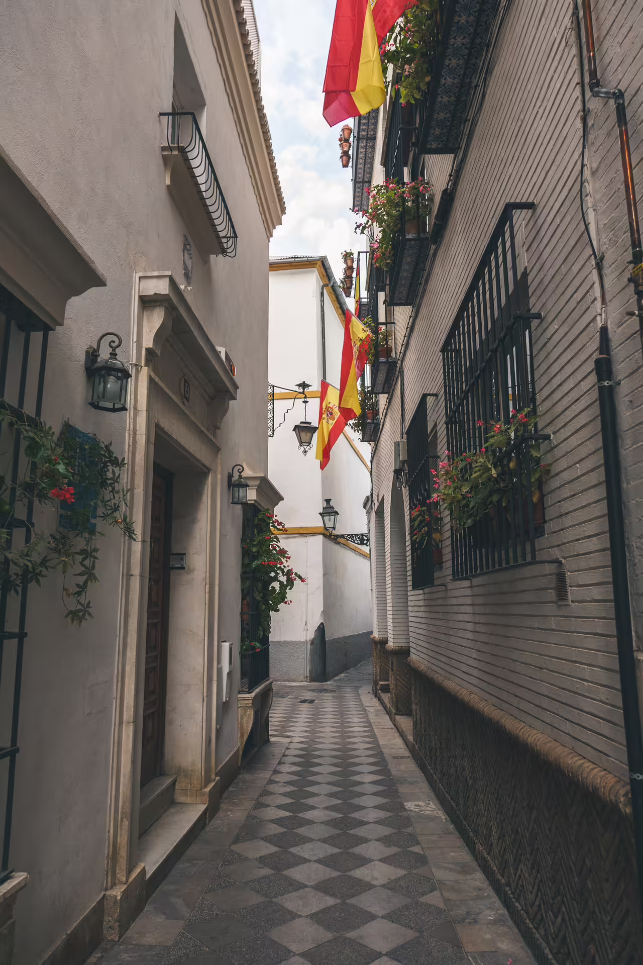 Narrow alley in Seville's Santa Cruz with Spanish flags and traditional architecture.