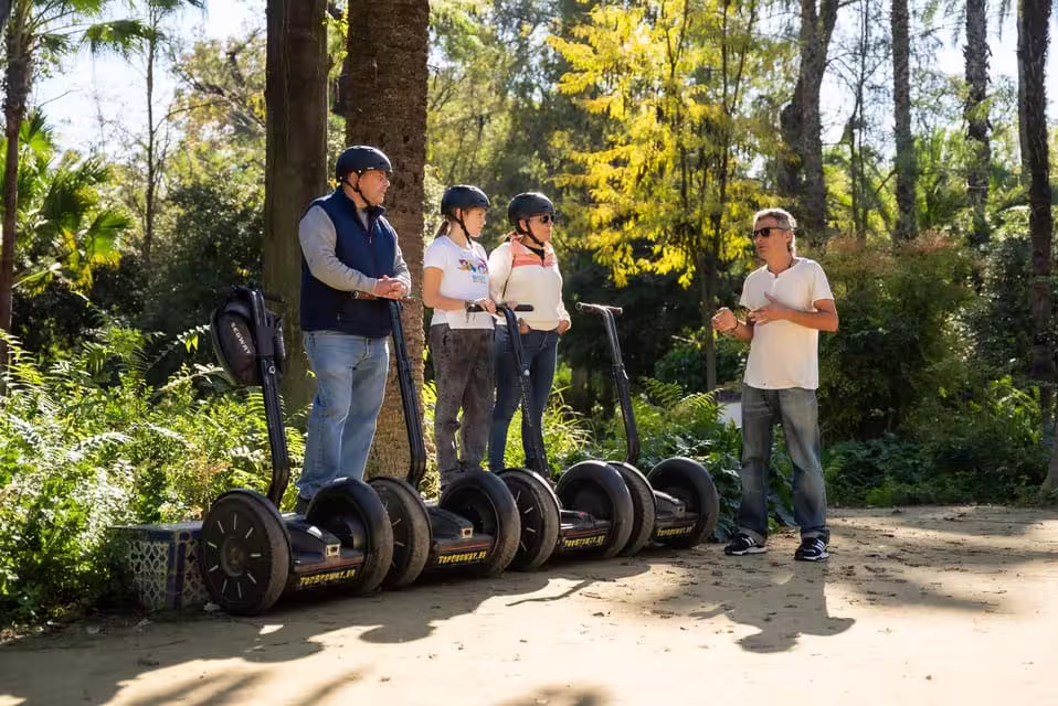 Tour guide explaining Segway use to tourists in a lush park setting during a Seville city tour.