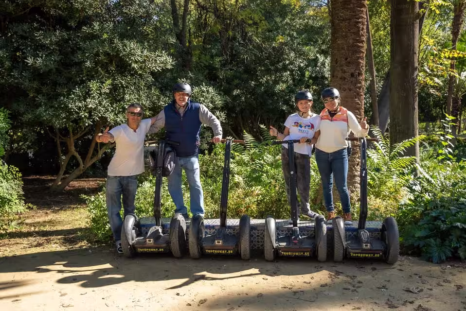 Smiling group on Segways poses in Seville's scenic riverside park, enjoying a guided 90-minute city tour.