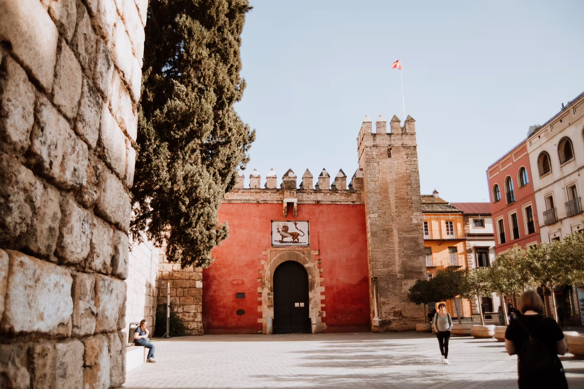 Tourists explore the historic Alcázar of Seville, featuring its iconic red walls and medieval architecture, on a guided walking tour.