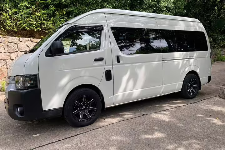 White transfer van parked on a sunny road in Seychelles, ideal for airport and hotel transfers, surrounded by lush greenery.