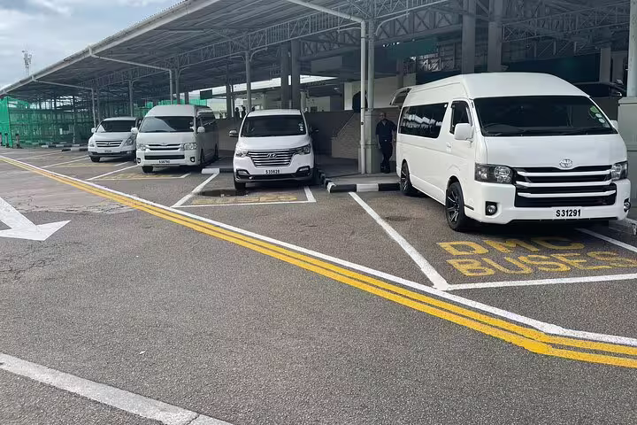 Row of white transfer vans lined up at Seychelles airport, ready for one-way hotel or airport transfer services.