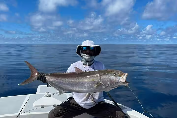 Fisherman displaying large amberjack caught during Seychelles deep-sea fishing excursion under clear skies.