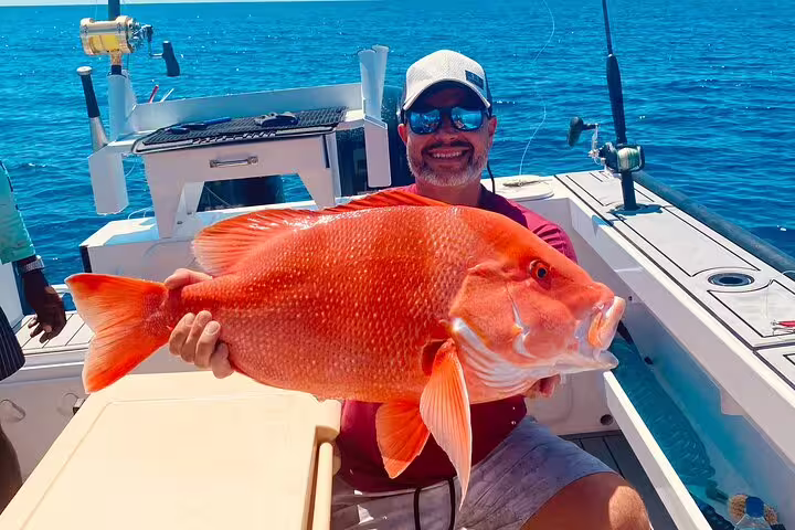 Fisherman holds large red fish on a Seychelles fishing expedition, showcasing a successful catch.