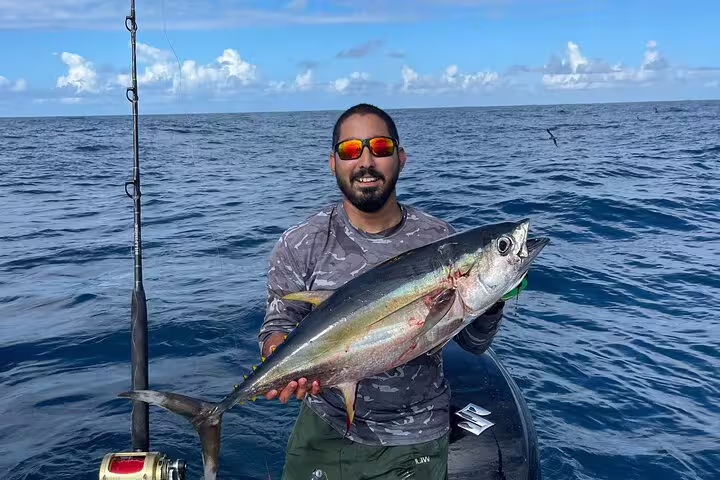 Excited fisherman showcasing a freshly caught tuna on a Seychelles fishing expedition, under clear blue skies.