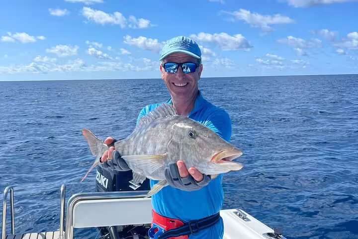 Happy angler proudly holding a large catch on a fishing boat in the deep blue waters of Seychelles.