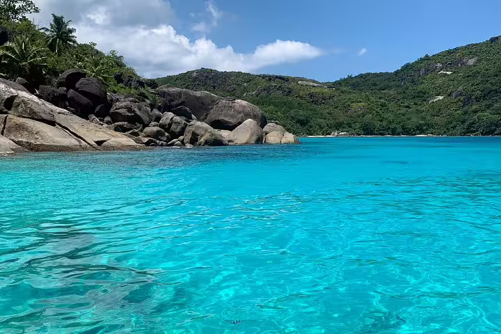 Turquoise waters meeting rocky shores at Anse Major, set against a backdrop of green hills under a blue sky.