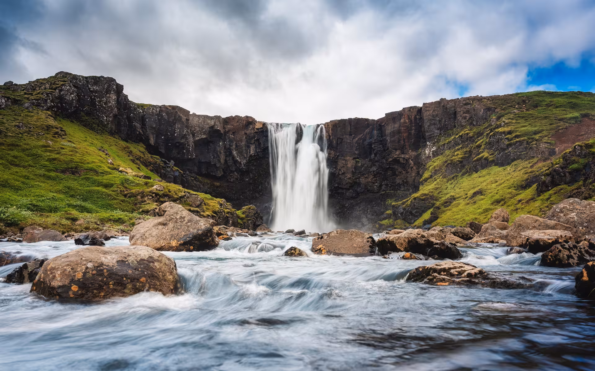 Stunning waterfall cascading over basalt cliffs into a rocky river in the Eastfjords of Iceland