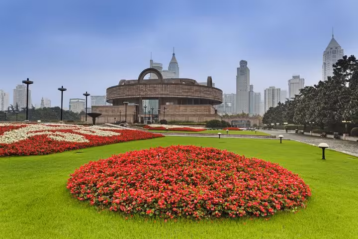 Shanghai Museum with red flower gardens in People's Square, surrounded by city skyscrapers