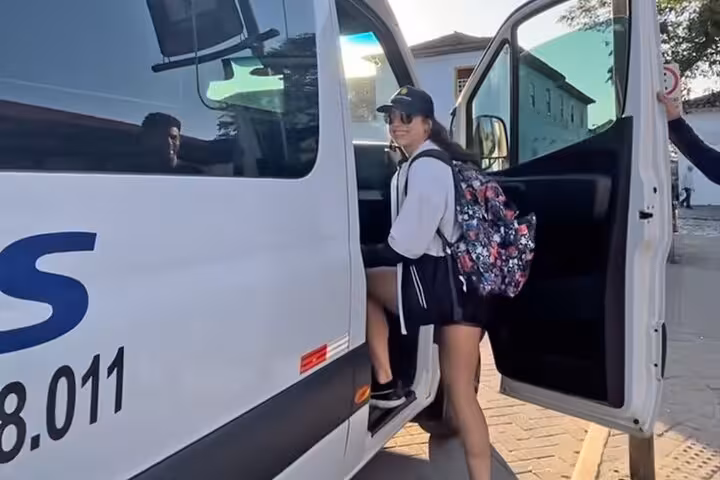 A traveler with a backpack boards a shared shuttle van, preparing for the journey from Ilha Grande to Paraty.