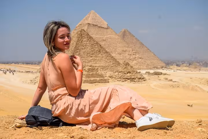 Traveler sitting in desert with Giza Pyramids behind on Sharm El Sheikh to Cairo air tour with Egyptologist guide