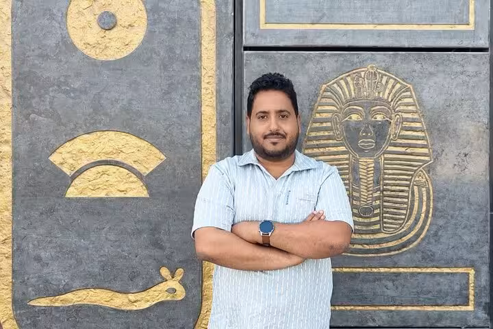 Tour guest posing by pharaoh relief at Grand Egyptian Museum, Cairo day trip from Sharm El Sheikh