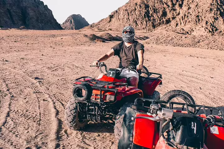 Rider on red quad bike in Sharm El Sheikh desert mountains on safari tour with Bedouin dinner and camel ride