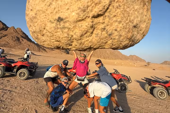 Friends posing with a giant rock during Sharm El Sheikh quad biking desert safari, ATVs and Sinai hills behind