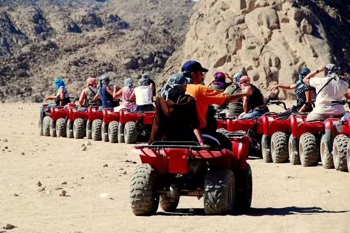 Group of riders on red ATVs in Sinai mountains during Sharm El Sheikh quad biking desert safari with camel ride