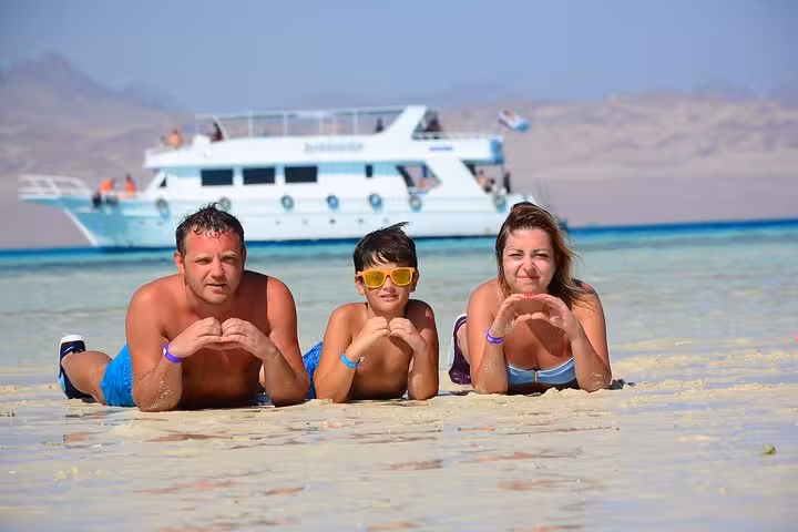 Family relaxing on White Island sandbar with yacht behind, Ras Mohamed snorkeling trip from Sharm El-Sheikh