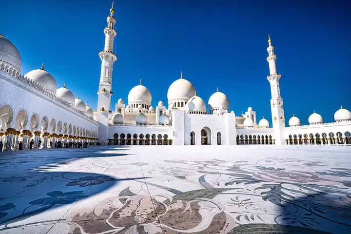 The stunning white domes and intricate architecture of Sheikh Zayed Grand Mosque in Abu Dhabi under a vibrant blue sky.