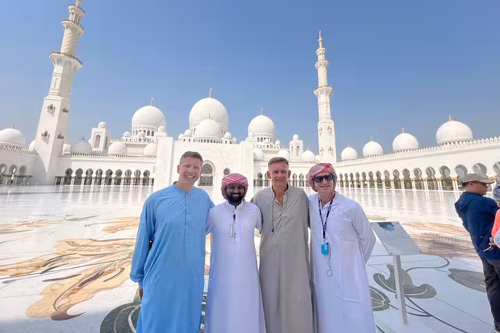 Tourists posing at Sheikh Zayed Grand Mosque on Abu Dhabi city tour, iconic white domes and courtyard