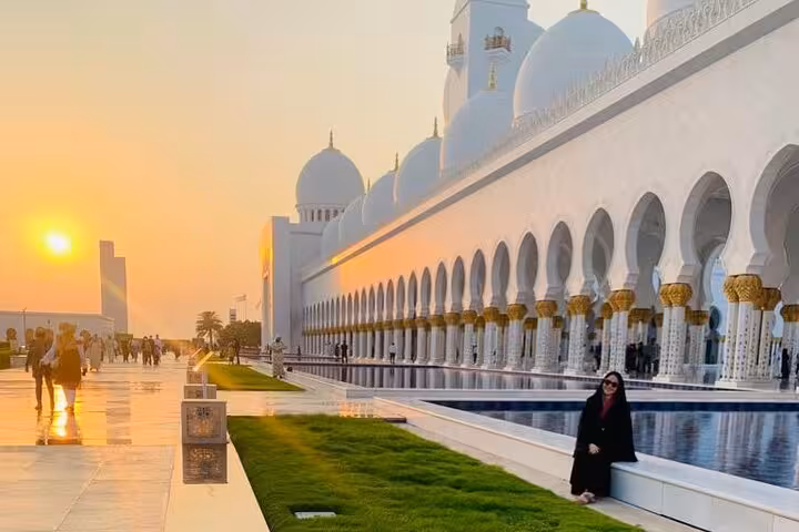 Tourist posing at Sheikh Zayed Grand Mosque during golden sunset on a full-day Abu Dhabi tour