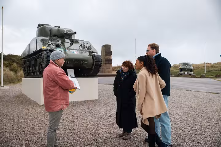 Tour guide explaining D-Day history to group near Sherman tank at Normandy beach memorial
