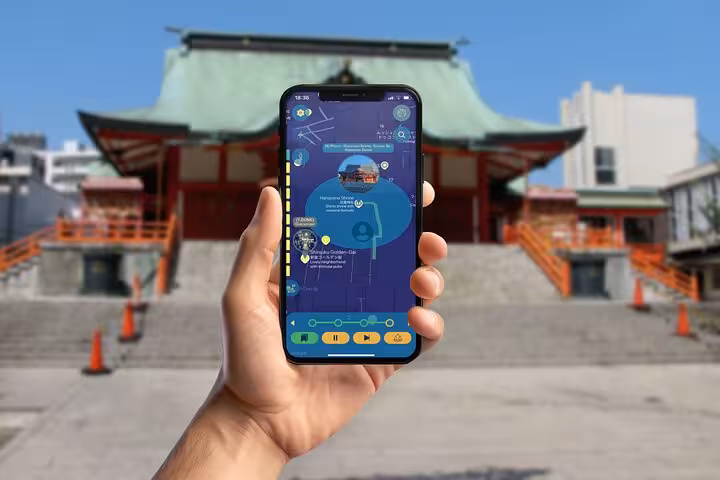 Hand holding smartphone with Shinjuku self-guided walking tour app in front of a Japanese shrine