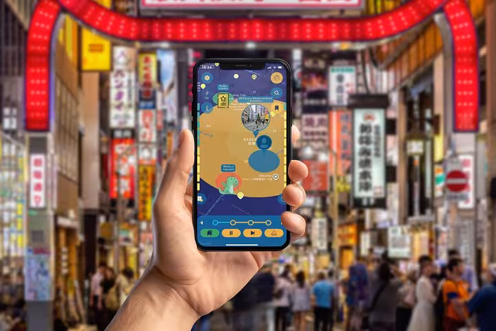 Hand holding smartphone with Shinjuku walking tour app map in busy Kabukicho street, Tokyo