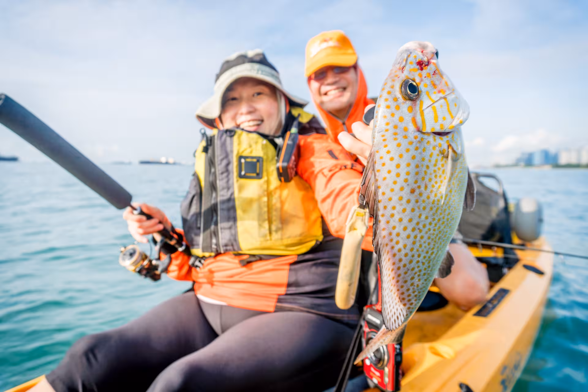 Happy couple showcases a vibrant fish caught during kayak fishing at Shipwreck Bay, Marine East.