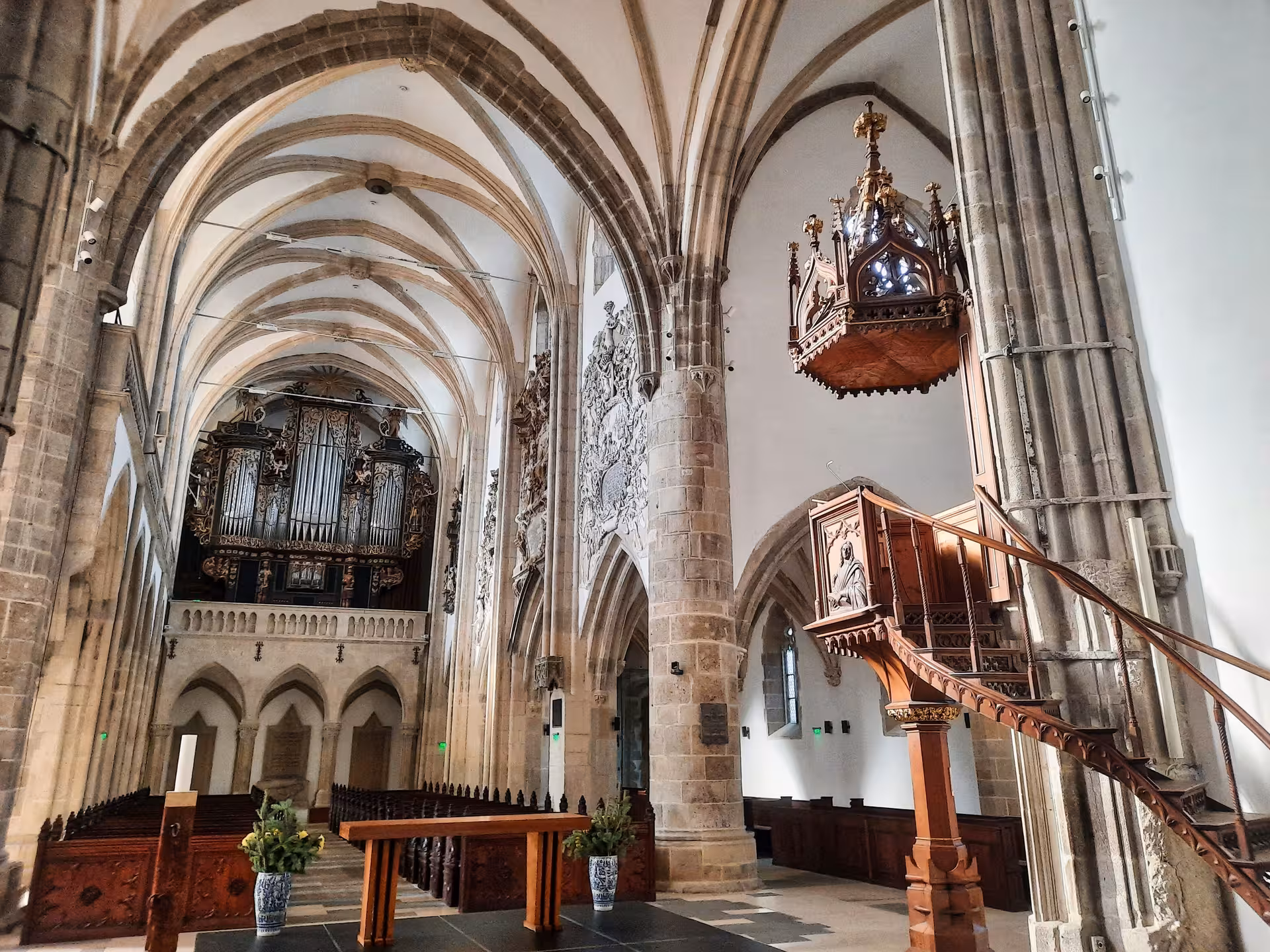 Gothic vaulted interior of a Sibiu church with ornate wooden pulpit and baroque pipe organ