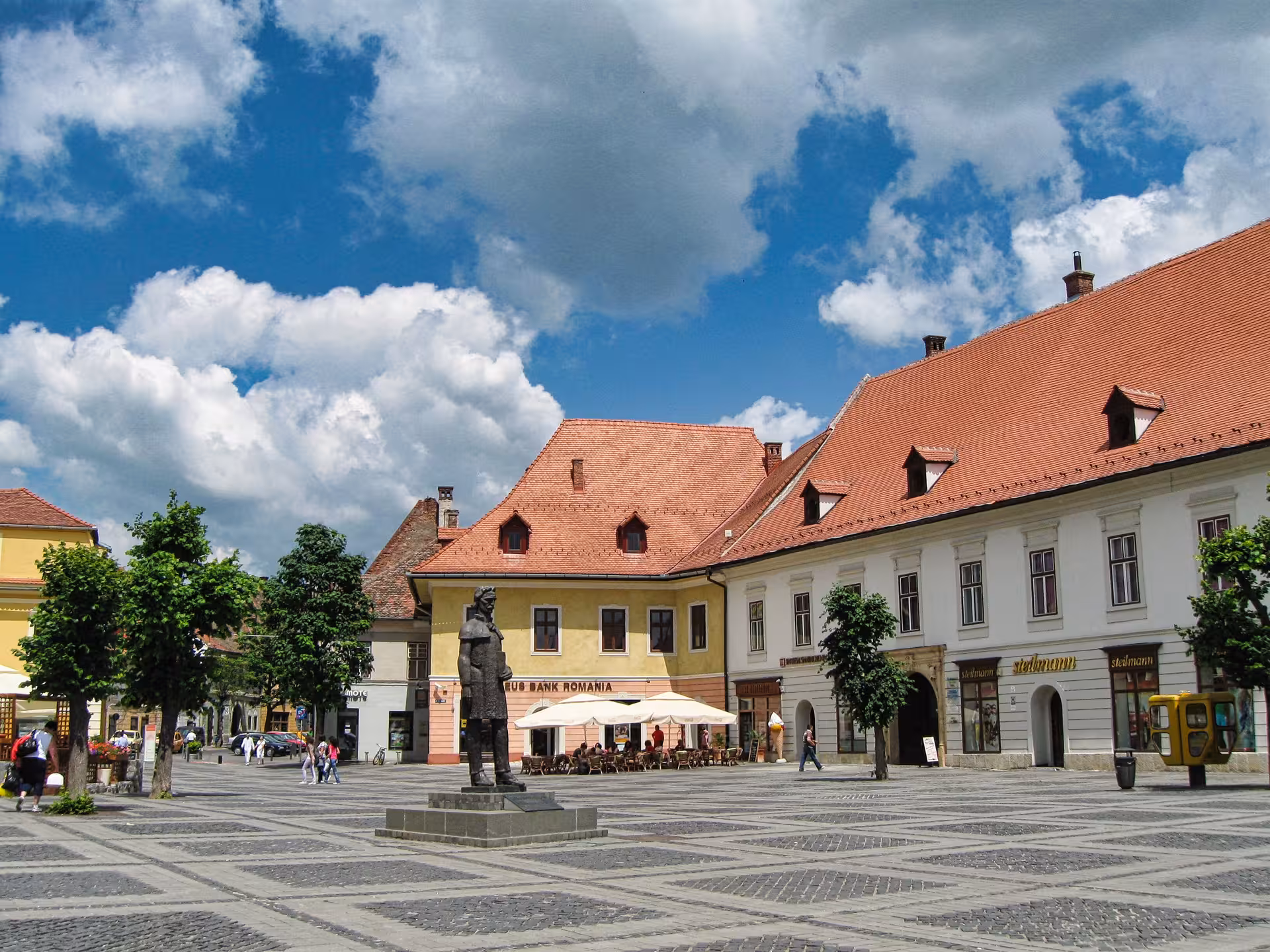 Sibiu Grand Square with bronze statue and historic Saxon buildings on a Corvin Castle day trip from Cluj-Napoca