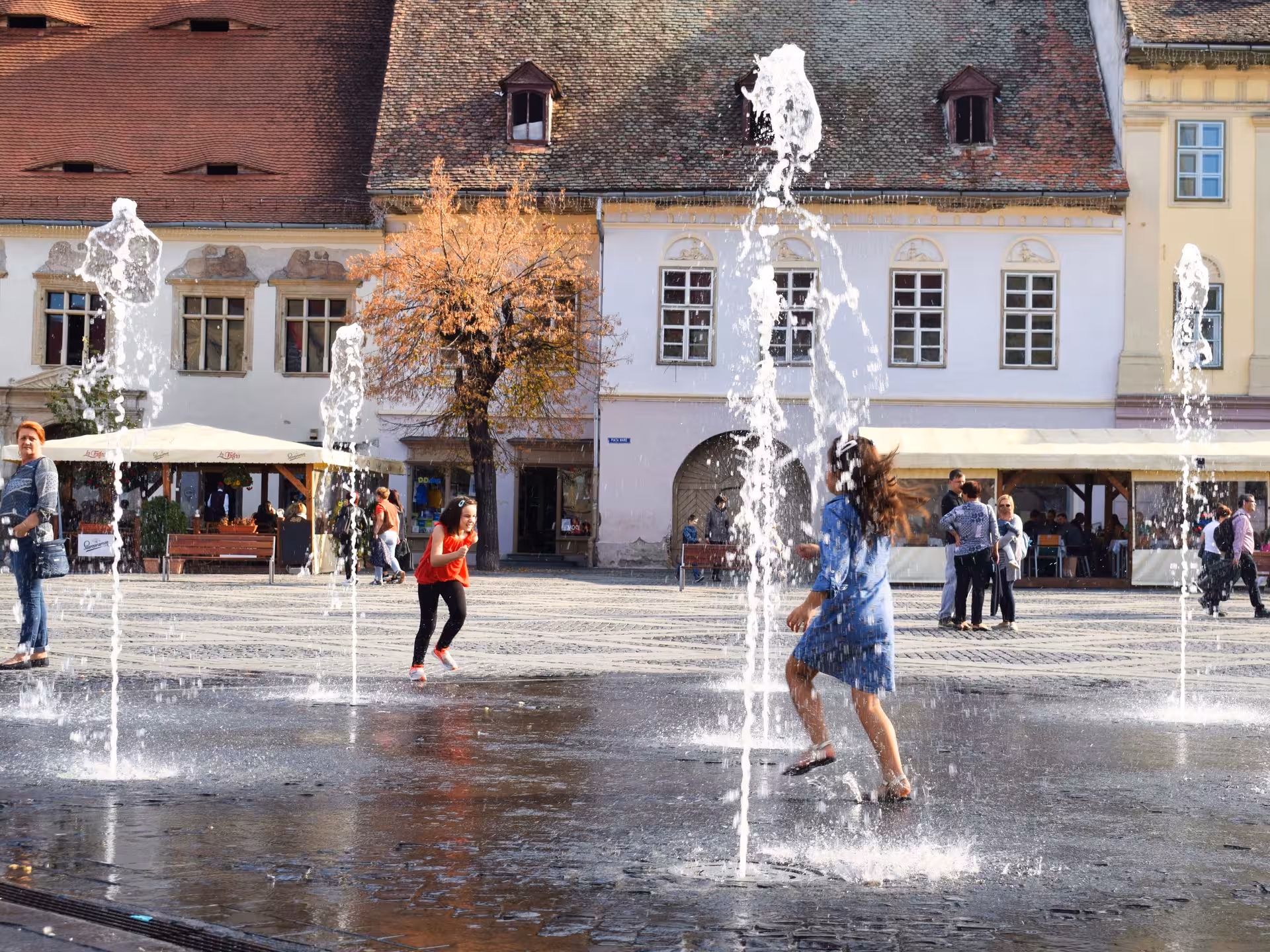 Girls playing in fountain jets at Sibiu's Grand Square with historic buildings in background