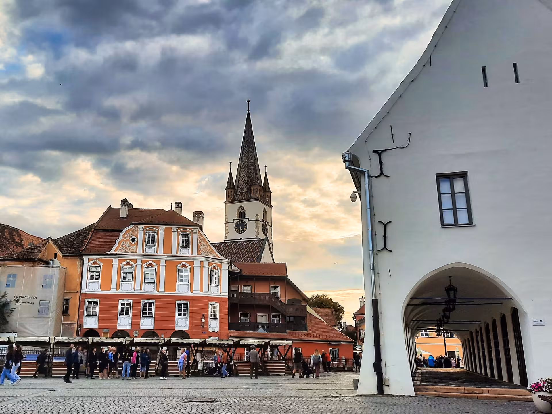 Sibiu historic square with colorful baroque buildings and Lutheran cathedral tower at sunset
