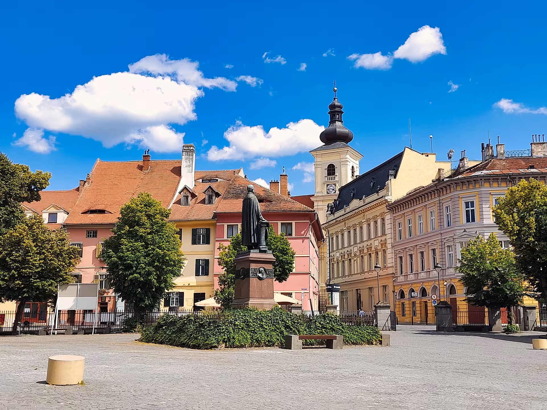 Sibiu historic small square with bronze statue colorful baroque buildings and church tower on a sunny day trip from Cluj-Napoca