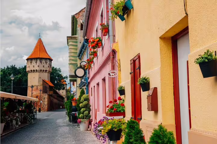 Colorful historic street with flower-adorned buildings and medieval tower in Sibiu Old Town, Romania