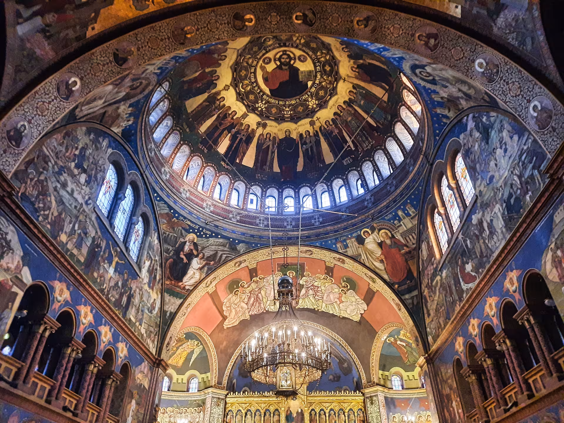Ornate Orthodox cathedral interior in Sibiu with Byzantine frescoes, golden dome, and chandelier