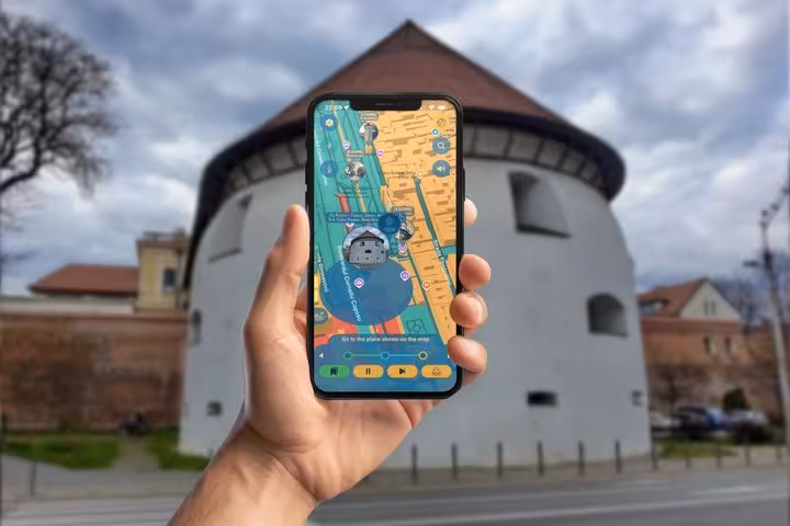 Hand holding smartphone with interactive tour map app in front of a round white historic tower in Sibiu