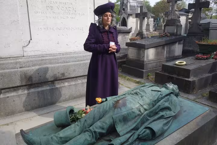 Woman in purple Victorian coat standing beside bronze statue grave at Pere Lachaise Cemetery Paris