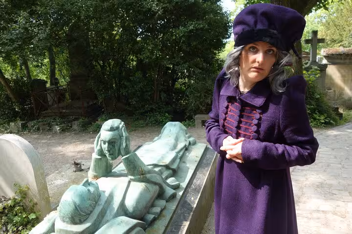 Woman in purple coat and beret poses beside bronze tomb sculpture at Père Lachaise Cemetery