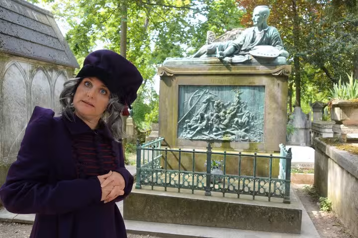 Woman in purple coat and black beret stands before ornate tomb at Pere Lachaise Cemetery Paris