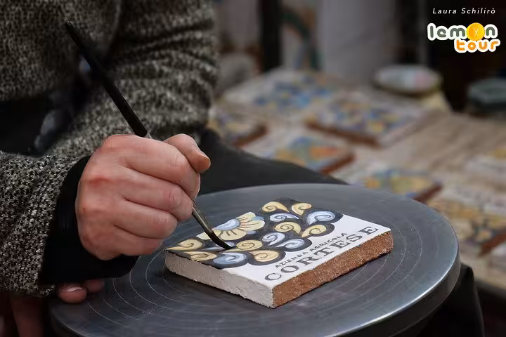 Artisan hand-painting a traditional ceramic tile in Caltagirone, showcasing intricate Sicilian craftsmanship.