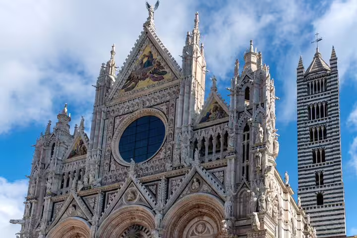 Ornate Gothic facade of Siena Cathedral with striped bell tower against blue sky