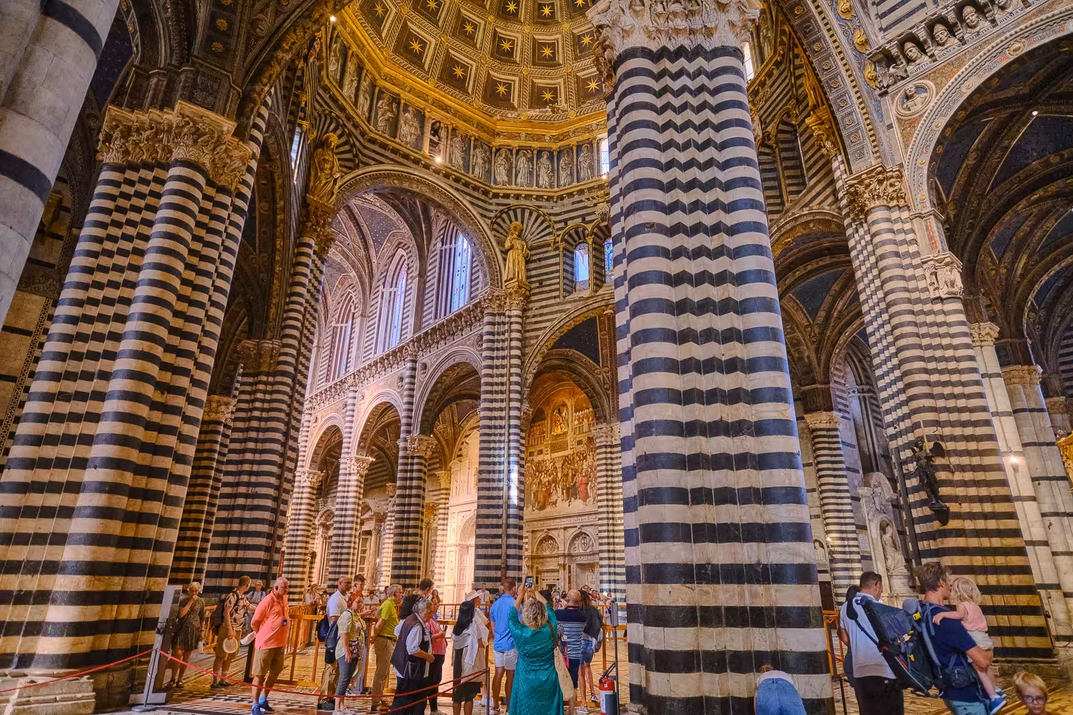 Visitors exploring the grand interior of Siena Cathedral, surrounded by its famous striped columns and intricate architecture.