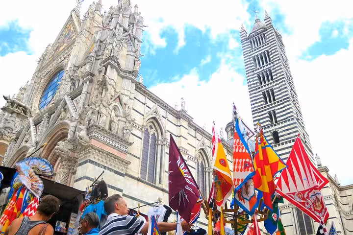 Vibrant flags and tourists in front of Siena Cathedral's intricate facade during a Tuscan small group tour.