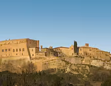 Medieval hilltop village with stone buildings and fortified walls under a clear blue sky in Siena, Tuscany