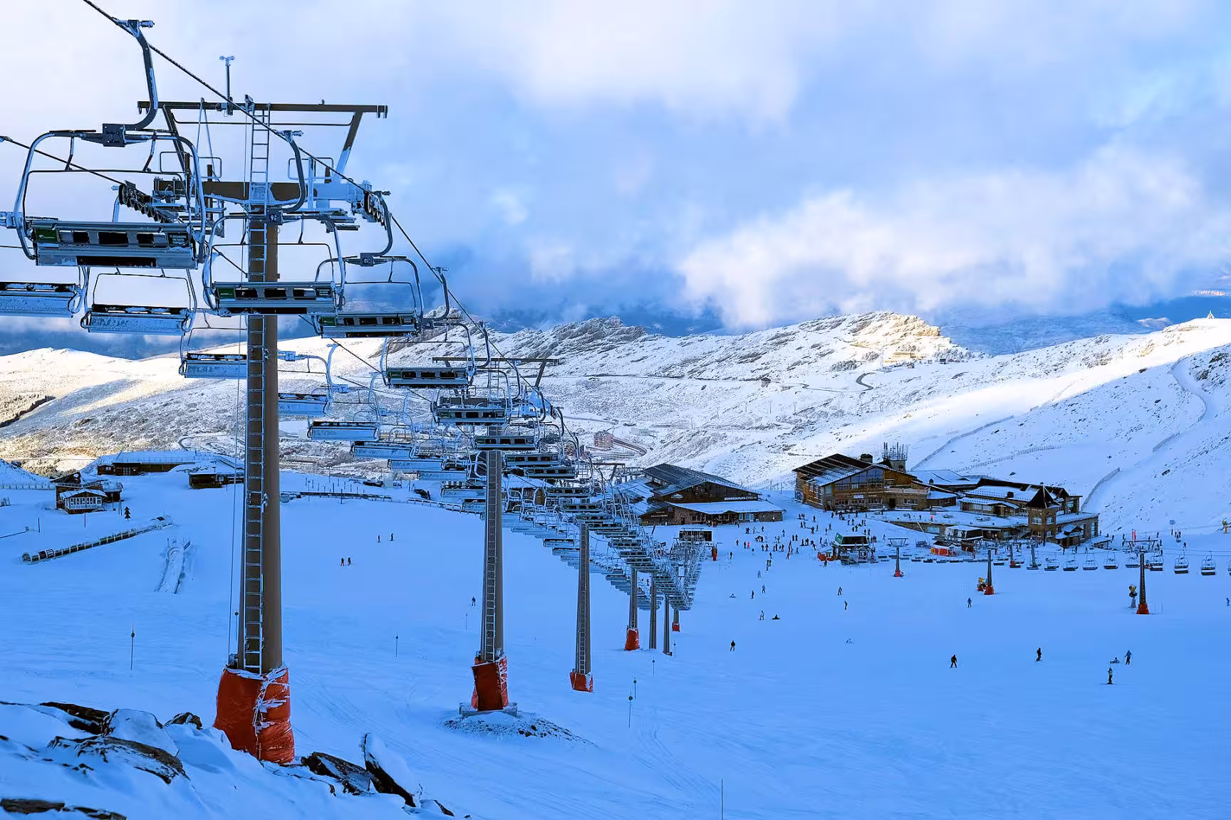 Sierra Nevada ski area featuring bustling chairlifts and skiers on snowy slopes with a cloudy mountain backdrop.