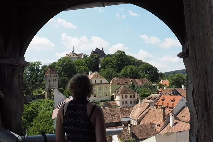 Traveler overlooking Sighisoara medieval citadel rooftops and hilltop church from a stone archway