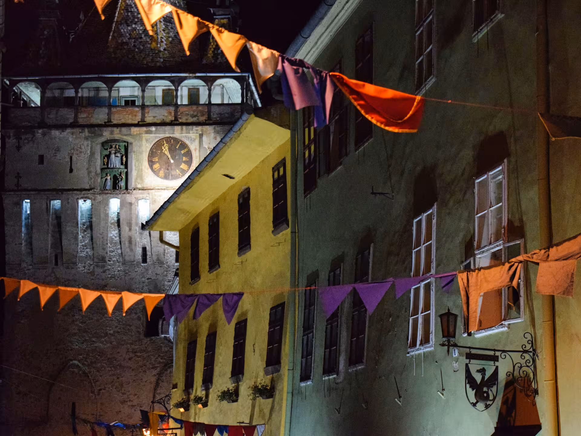 Sighisoara Clock Tower illuminated at night with colorful bunting flags in the medieval citadel