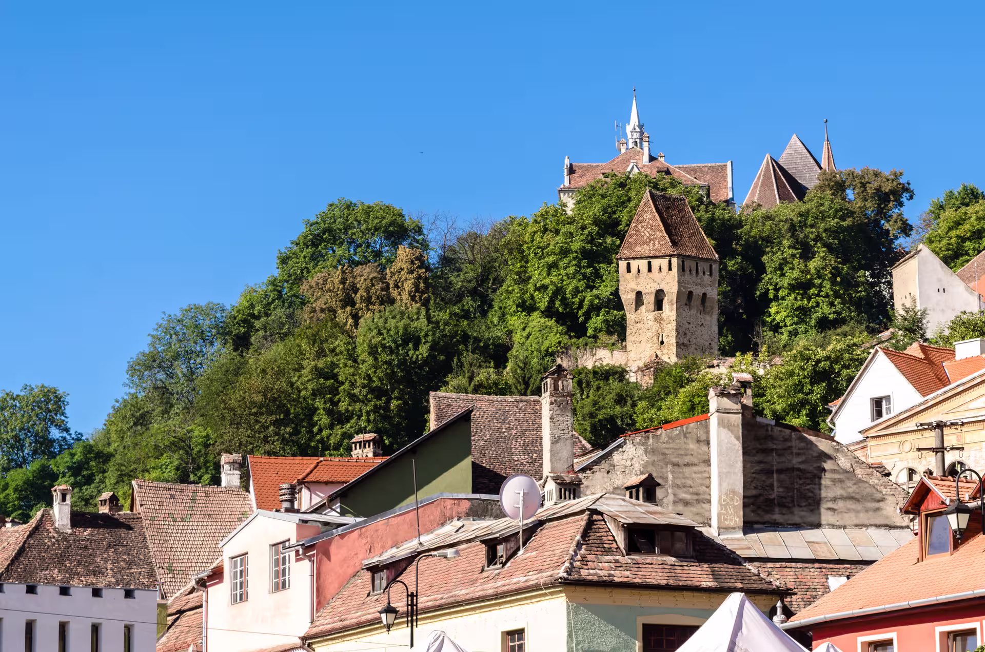 View of Sighisoara's historic towers and colorful rooftops under a vibrant blue sky, perfect for a Dracula candlelight tour.