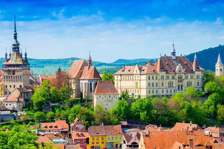 Aerial view of Sighisoara medieval fortress citadel with clock tower, historic buildings, and green hills in Transylvania